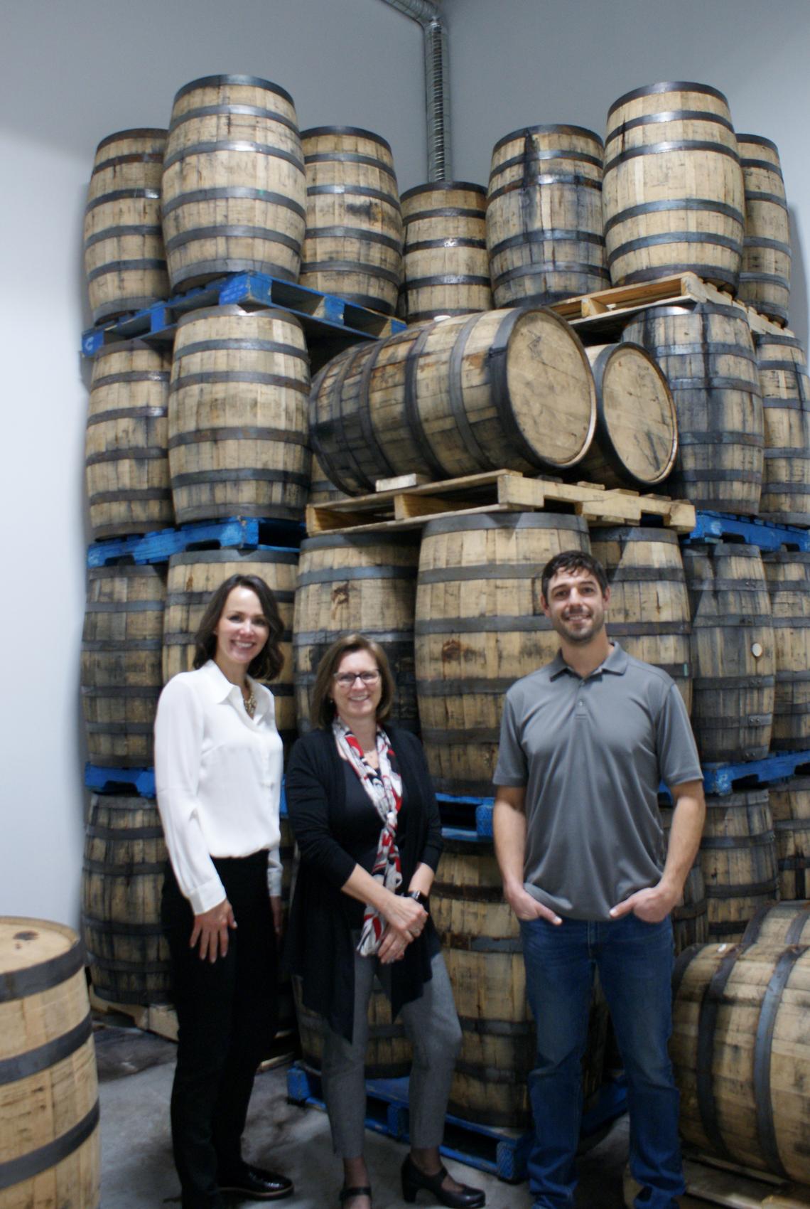 Leitha Cosentino, Director of Development, and Dr. Lesley Rigg, dean of the Faculty of Science, and Tomas Romero, pictured in front of casks at Romero Distilling.
