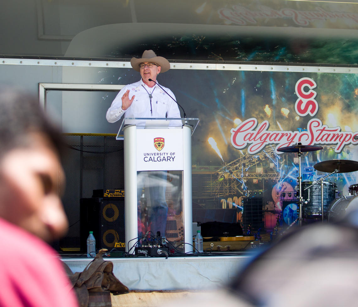 UCalgary President Ed McCauley speaks on a stage in front of the Calgary Stampede logo at the 2019 Barbecue..
