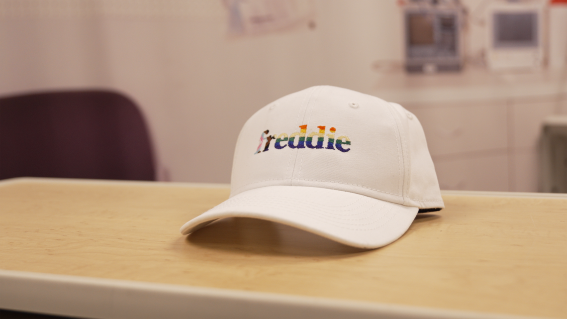 A white baseball hat with the Freddie logo sits on a table in a hospital room