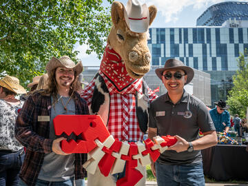 Mason Plested (Advancing Technologies technician) and Kevin Le (Mechanical Engineering technician) pose with a giant “flexi-Rex” and Stampede mascot Harry the Horse.