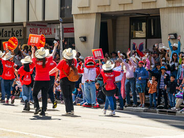 UCalgary volunteers marching at the Stampede Parade while UCalgary community members cheer from the bleachers. 