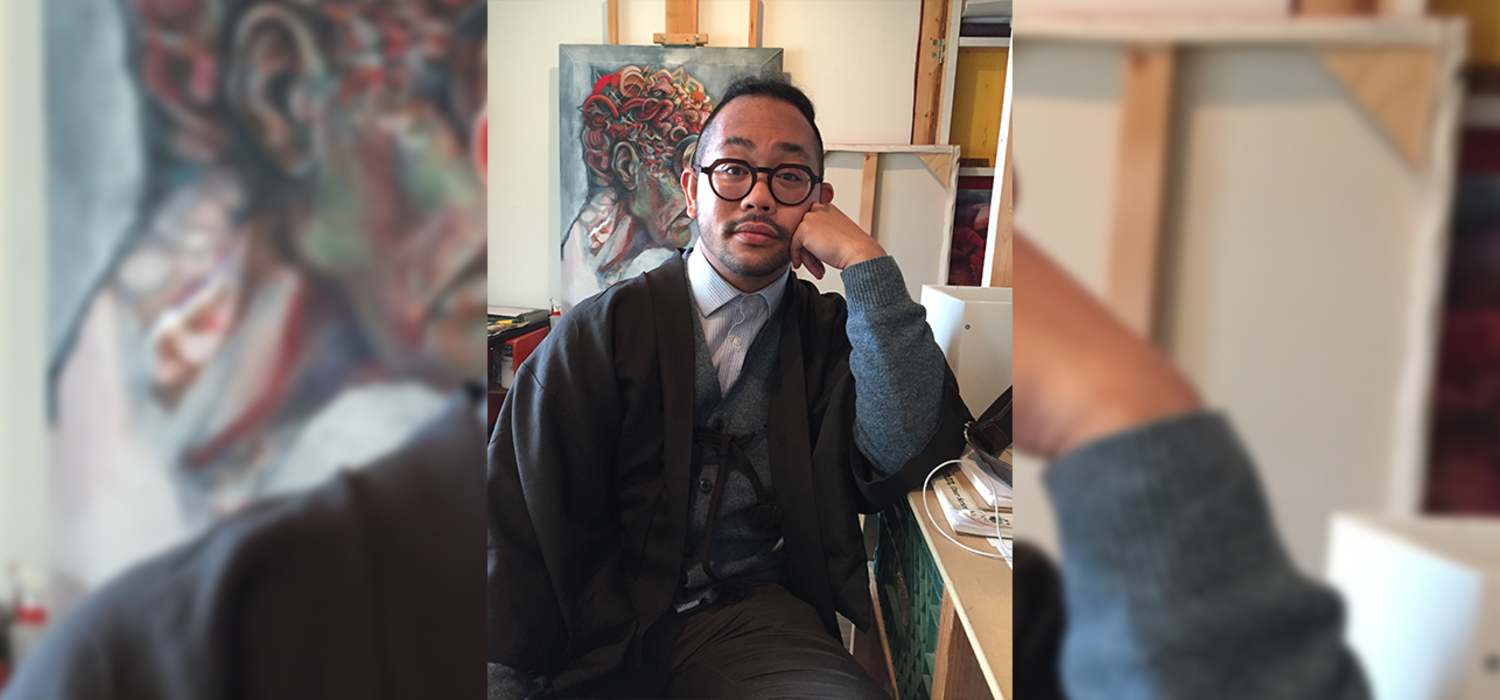 Alumnus Jordan Baylon sits in his Calgary Arts Development office. Paintings are scattered behind him.