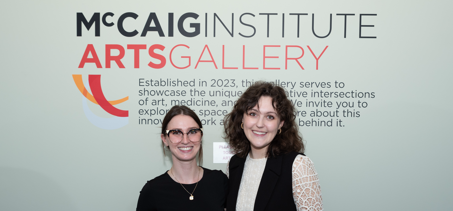 Two women stand together in front of the McCaig Institute sign