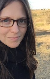 Alumna Caleigh Hanks stands facing the camera. A bare prairie is behind her.