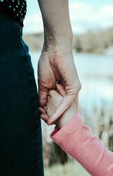 A child in a pink shirt holds hands with their parent.