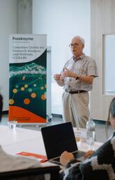 A man in a button down stands in front of a room full of people while giving a lecture