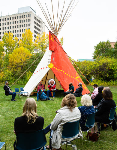 Students and staff sit in a circle around the UCalgary tipi at the Indigenous Orientation for law students
