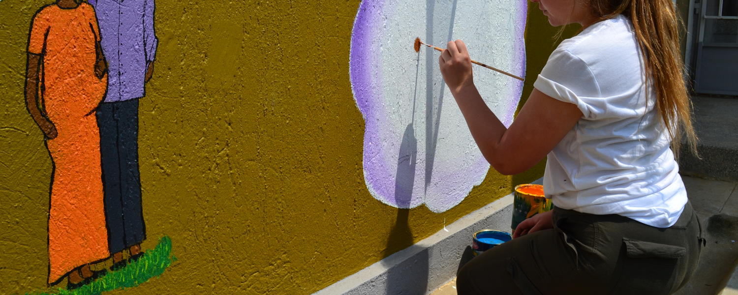 student painting a mural on a wall
