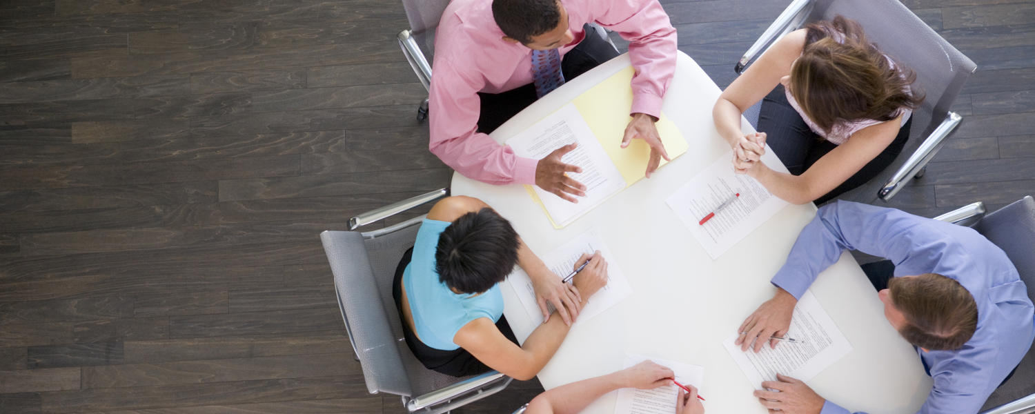 A birds eye view of 5 people seated at a a table collaborating on a project. 