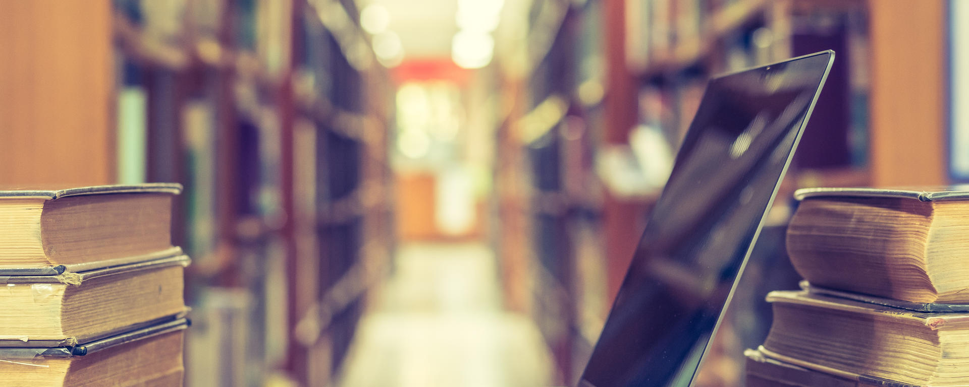 Library aisle and a table with a pc and books on it.