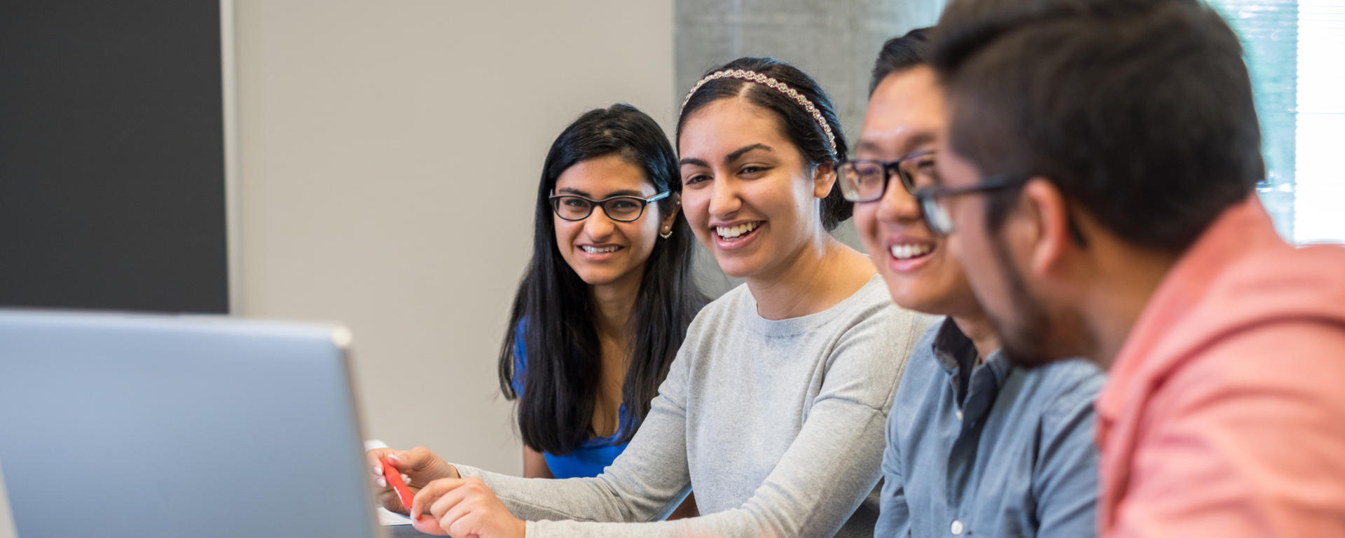 4 people gathered in front of a laptop collaborating