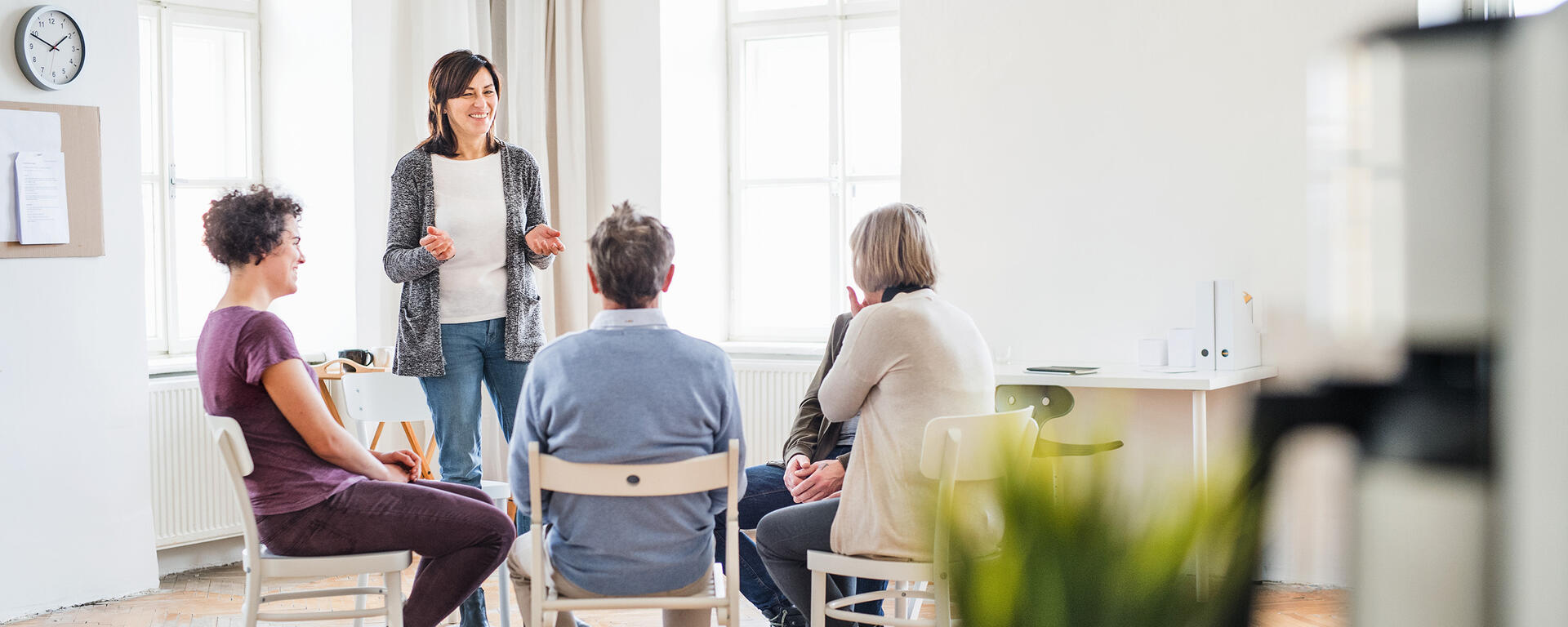 Stock photo of a group of people sitting together having a discussion. With one female standing and smiling