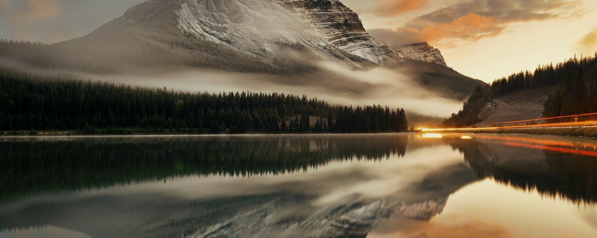 Mountain lake and traffic light trail with reflection and fog at sunset in Banff National Park, Canada.