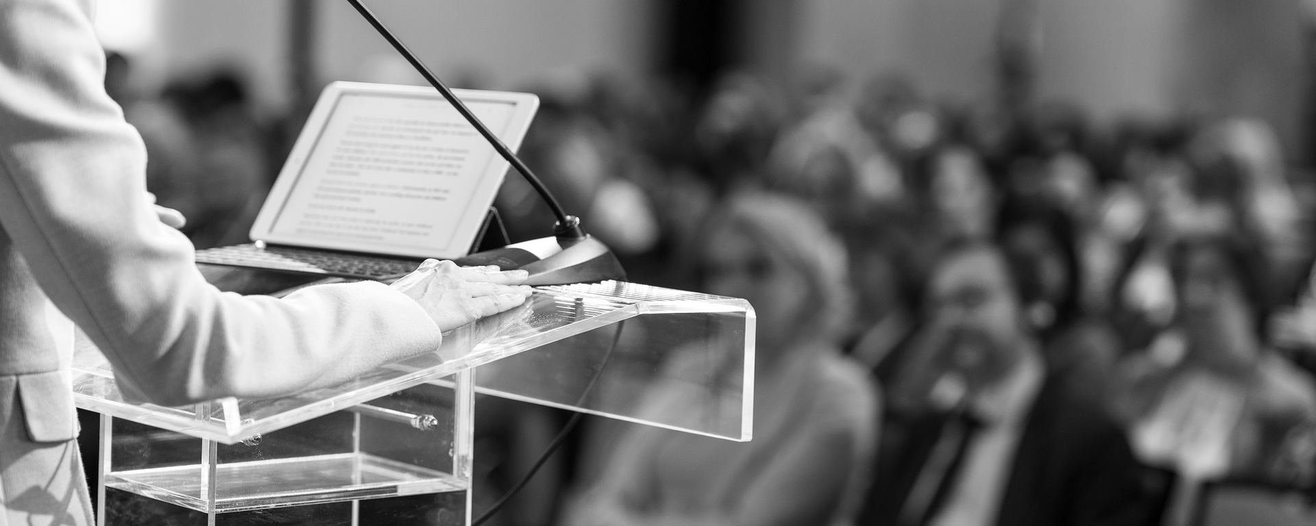 close up of a person standing at a podium facing the audience giving a presentation on a laptop