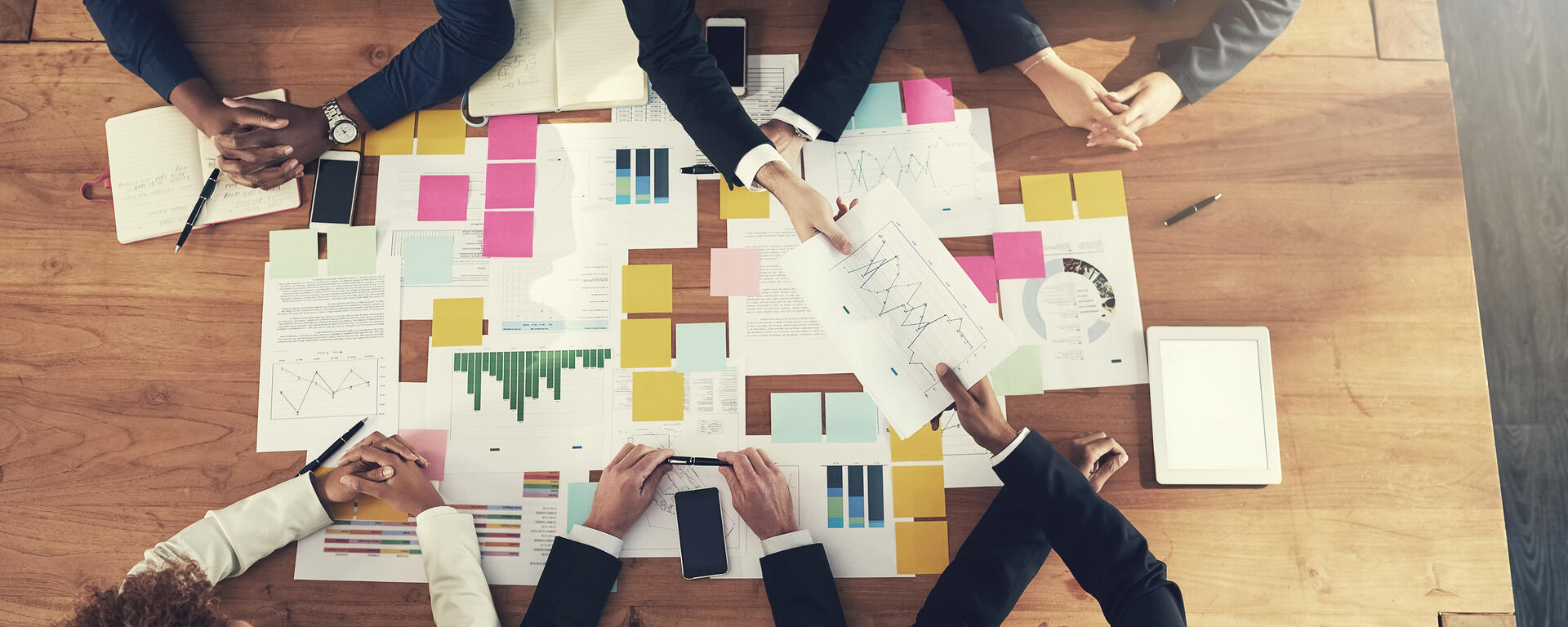 A group of professionals around a table filled with graphs, papers and charts. Looks like a working meeting, or a workshop