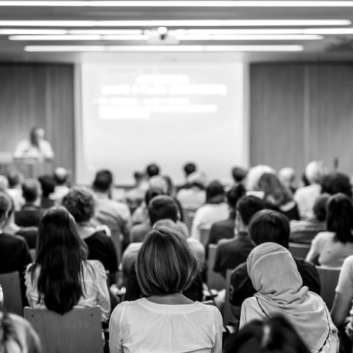 back and white photo of a crowd of people listening to a presentation 