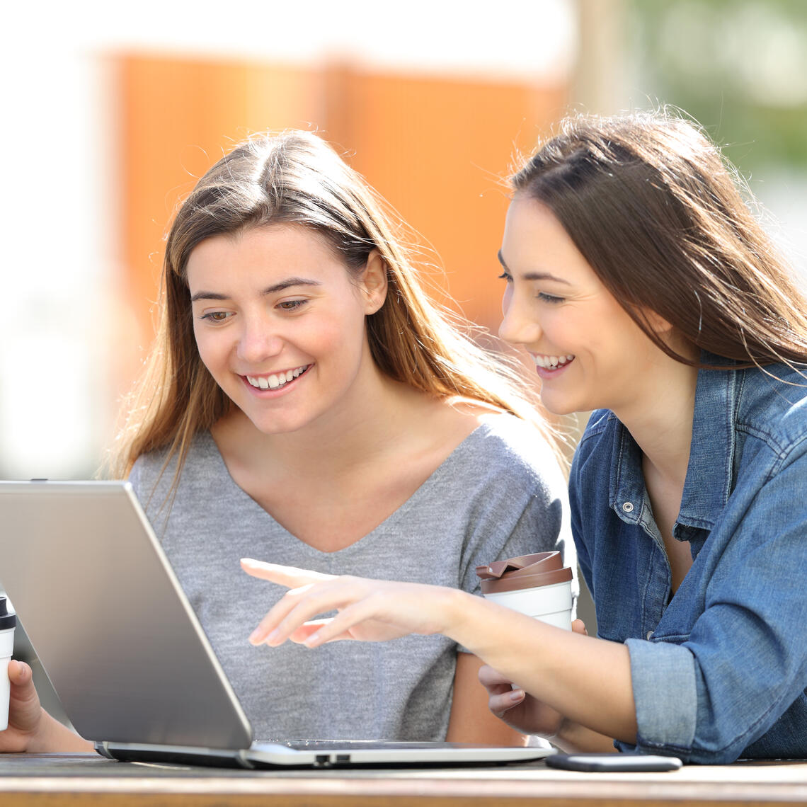 Two women are looking at a laptop screen smiling and in mid conversation 