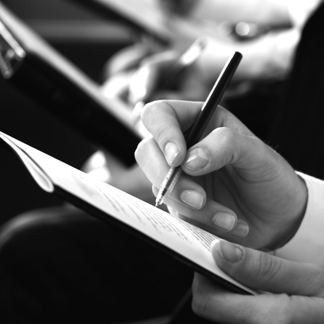 black and white photo of hands taking notes at a conference