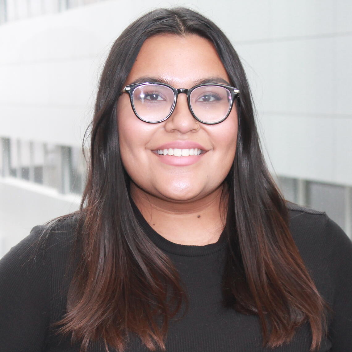 Sarina Ayral, Master's Student, smiling in a professional headshot with a blurred building background