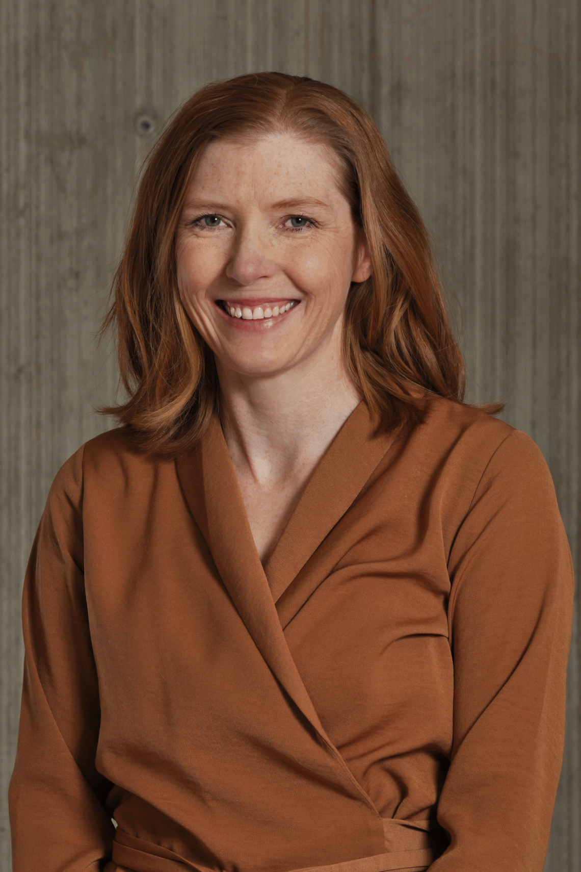 Professional photo of Dr. Kerry McBrien. Female, with red shoulder length hair. Wearing an orange blouse and smiling. 