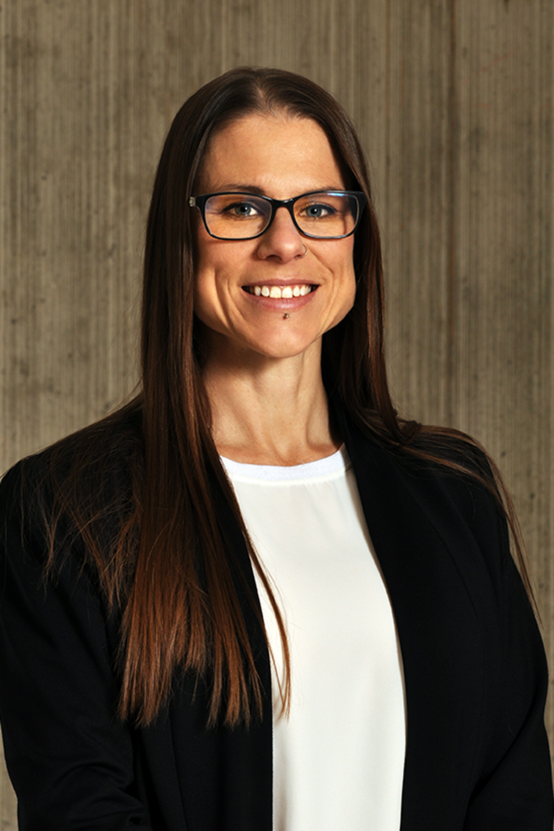 Professional photos of Sarah Gil, female, wearing glasses, with long hair and wearing a black jacket with a white shirt. 