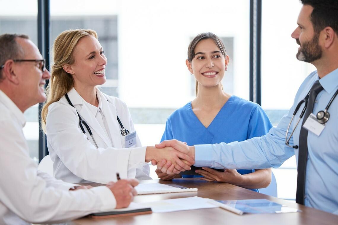 Male and female doctor shaking hands. Their colleagues, one male and one female standing close by and smiling