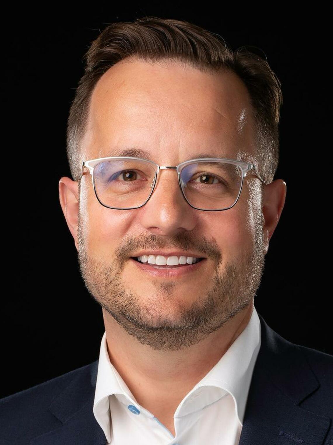 A photo of Derek Exner, a white man in his 40s smiling with glasses and short brown hair.