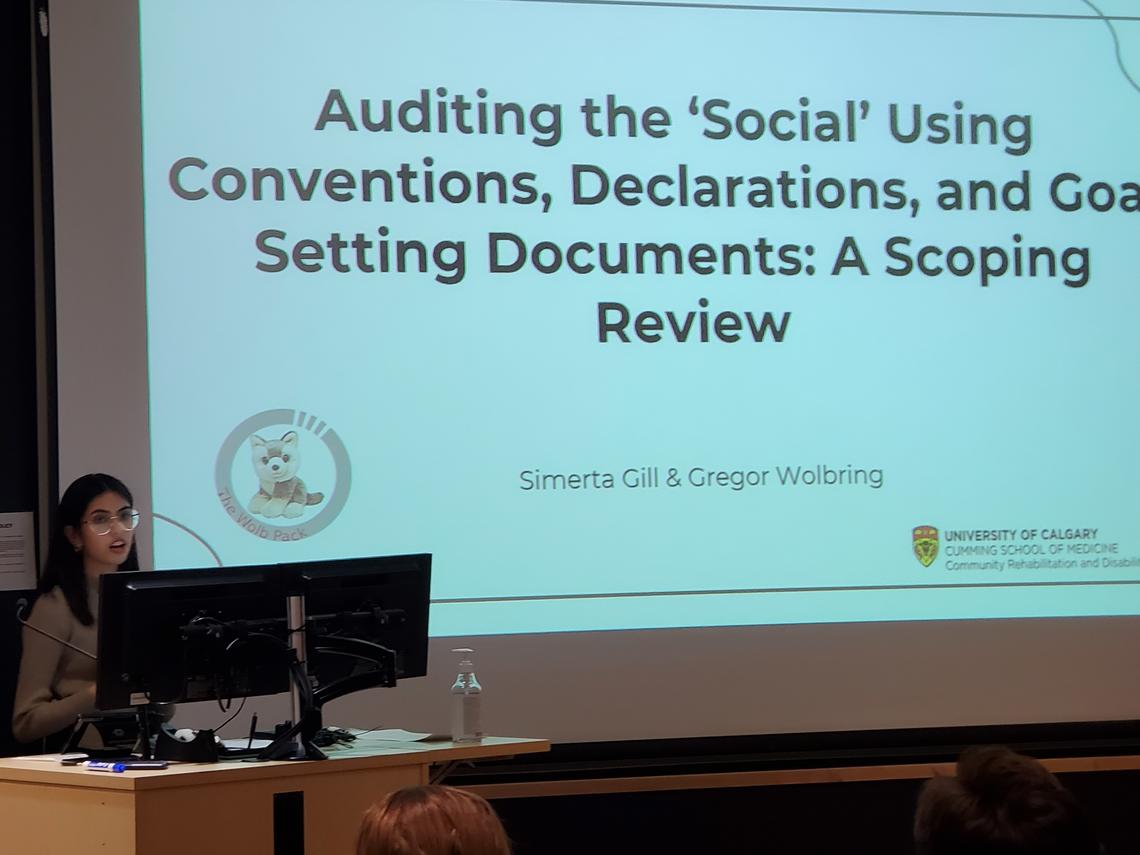 A student presents at the podium "Auditing the 'Social' Using Conventions, Declarations, and Goal Setting Documents: A Scoping Review