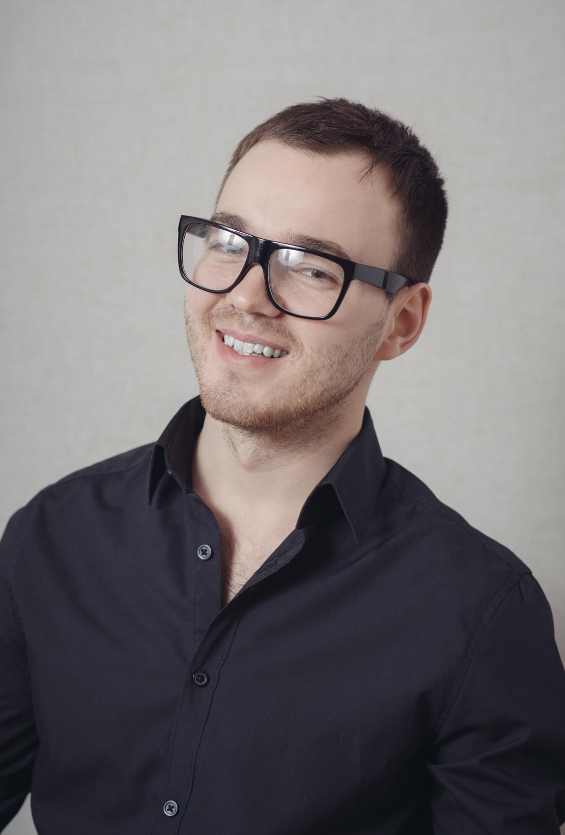 Man is smiling for portrait photo in glasses and long sleeve burgundy button up 