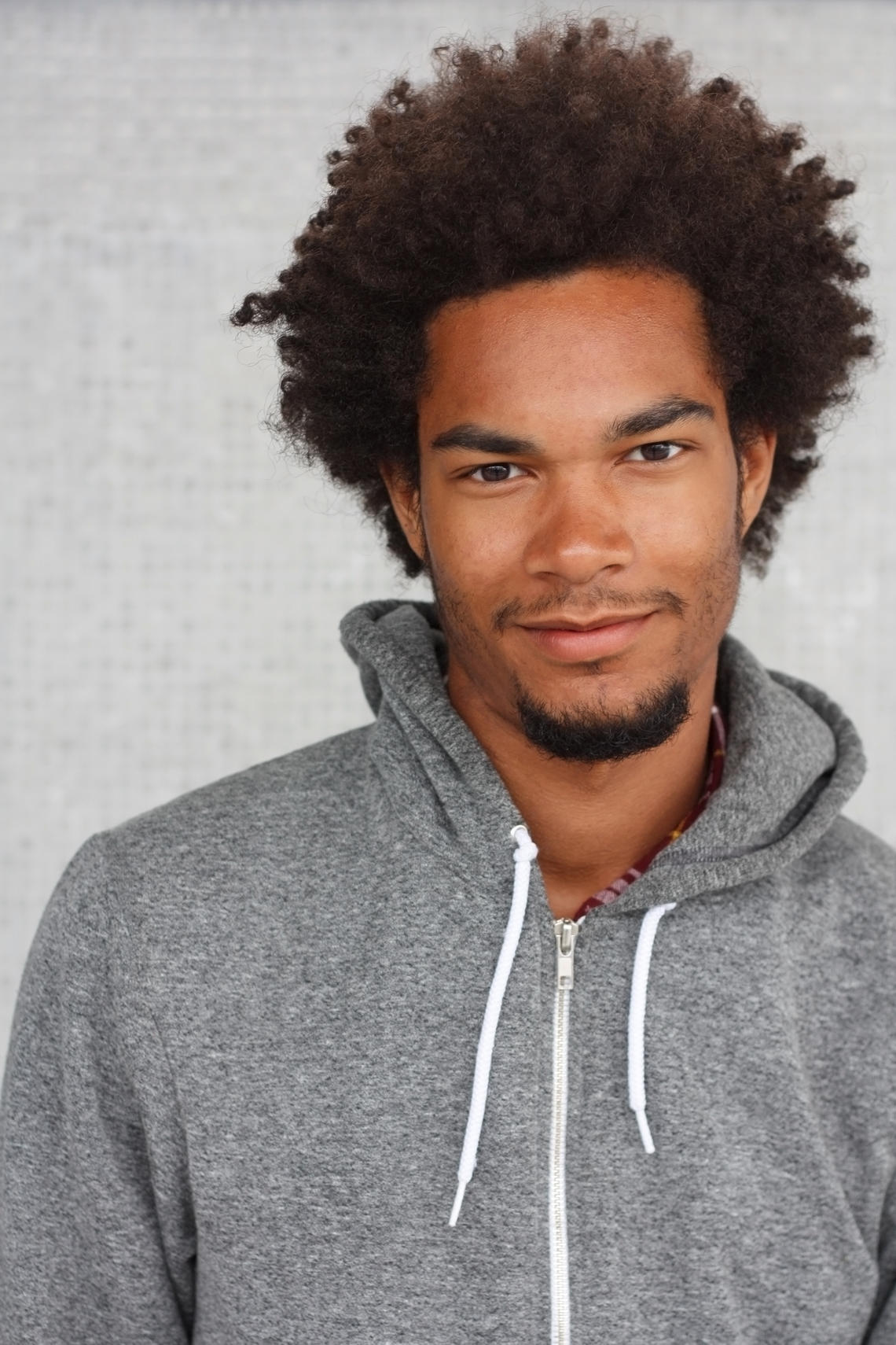Portrait of a Man smiling with curly black hair. He is wearing a grey hoodie