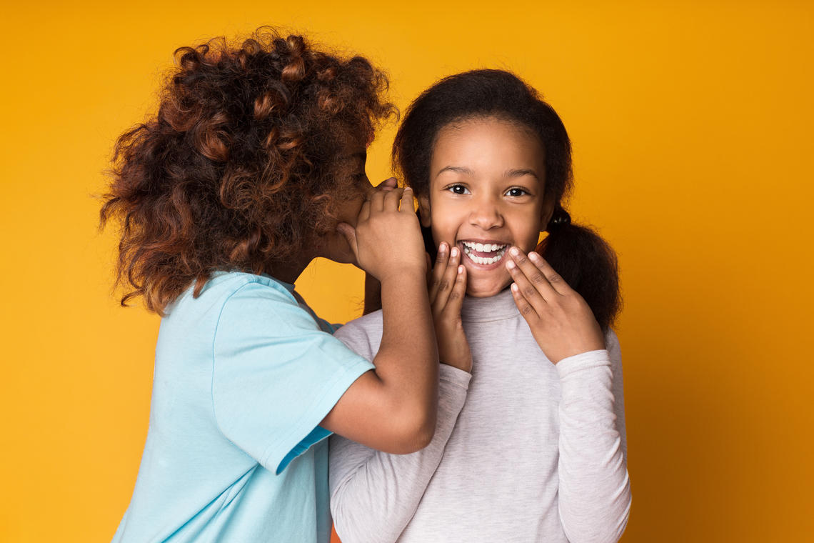 Young girl whispering in the ear of another girl