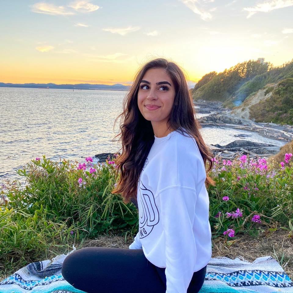 photo of Desiree Joozdani, sitting in front of an ocean and looking back at the camera
