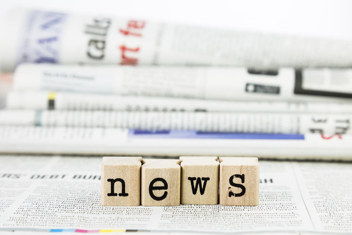 A photo of newspapers in the background. At the foreground the word "News" is spelt out via brown blocks