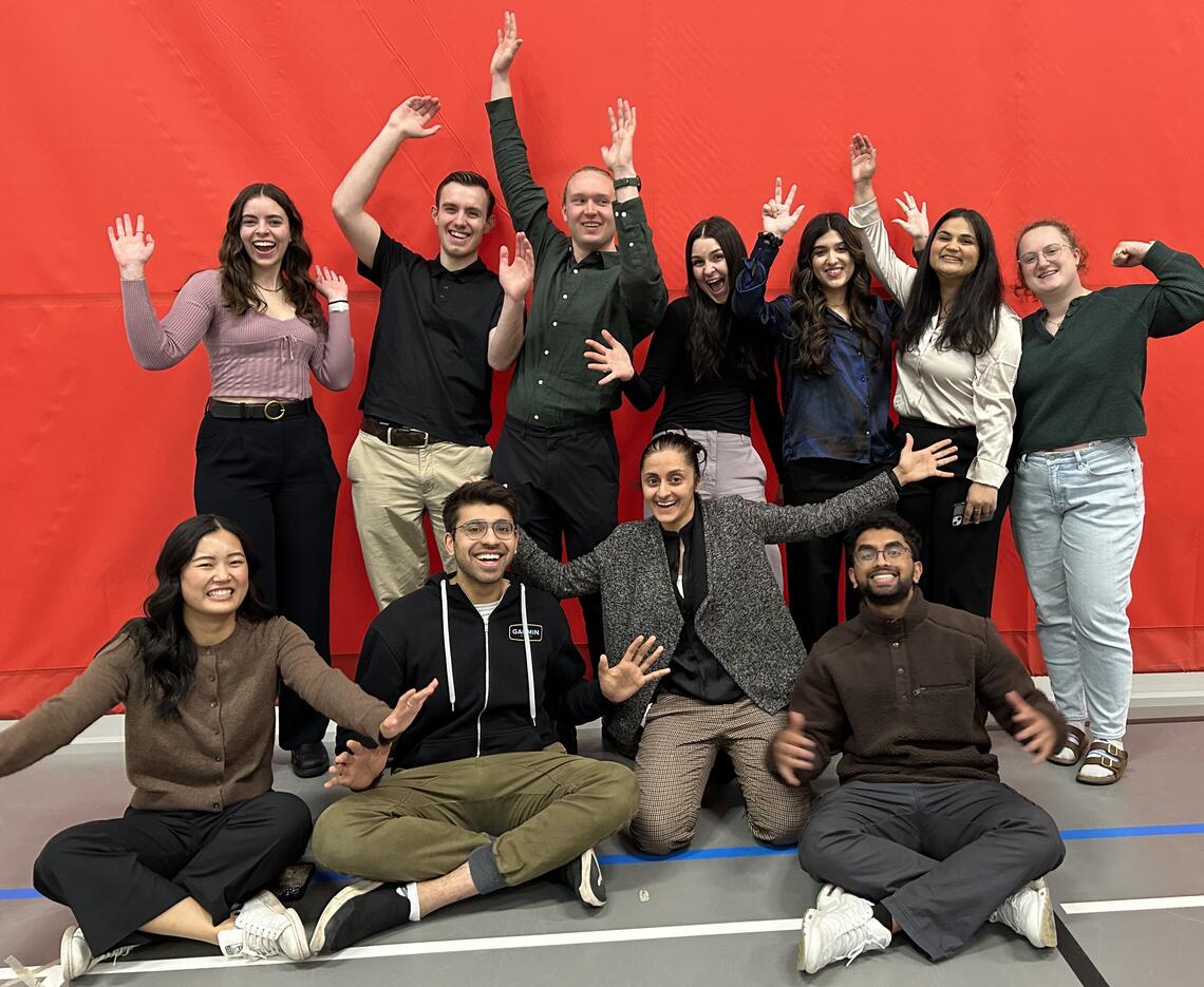 12 members of the lab research team, various genders and ethnicities, with their arms raised in the air and smiles on their faces