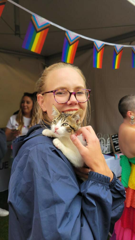 Caucasian female with glasses, blond hair in ponytail, navy blue hoodie, and holding a cat