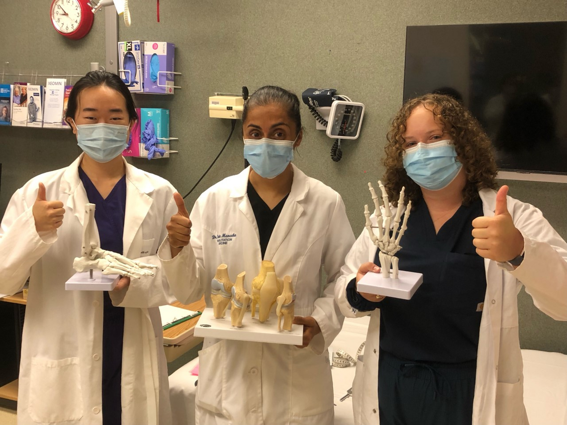 3 female scientists wearing white coats and holding models of upper body skeletal structures