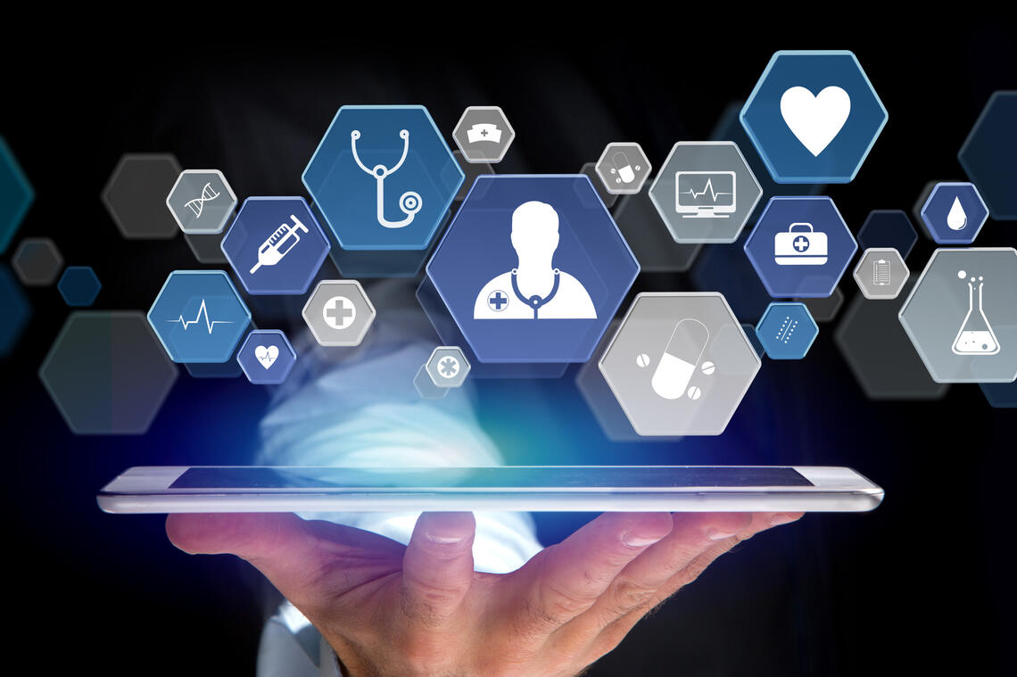 Ipad resting on a hand face up. Above the iPad are hexagon shapes with icons in them such as a doctor icon, a heart, a stethoscope. 