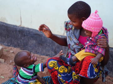 A mother plays with her child while waiting for a routine check up, Nyamayinza, Misungwi