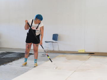 An artist priming the plywood boards with white paint