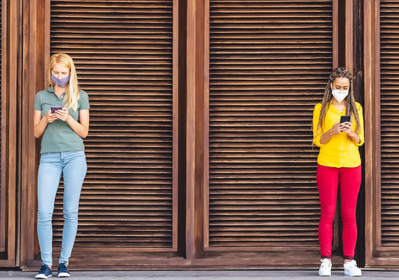 Two social distanced female teenagers using cell phones