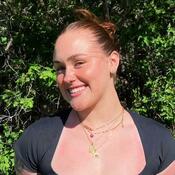 CRDSSA VP Finance Brittney Dunn. Brittney is has medium brown hair that is in a slick back bun. She is smiling in front of a green tree. She is wearing a black tee shirt and leopard pants. 