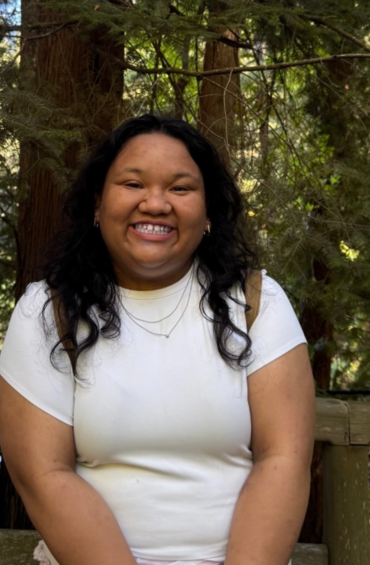 CRDSSA President Jemma Nombre. Jemma has shoulder length dark curly hair, she is smiling wearing two necklaces and a white tee shirt