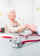 Red stethoscope on desk in doctor's office in front of elderly patient