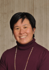 Headshot of Dr. Pamela Chu, wearing a plum-coloured sweater against a tan background