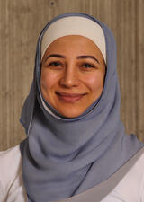 Dr. Heirali smiles into the camera. She is wearing a white hijab cap under a soft blue chiffon hijab and white top.