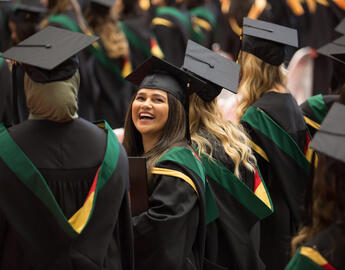 A picture of a group of graduates with a smiling woman looking towards the camera