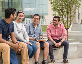 A group of four University of Calgary students sit outside on a bench